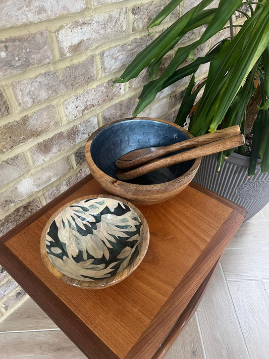 Small wooden bowl with floral design. Background colour an inky blue, green, black. With finger like leaf pattern. Alongside a medium size hand painted wooden bowl in a royal blue colour with pearl finish and fishscale design. Made of sustainable mango wood and suitable for cold and warm food.