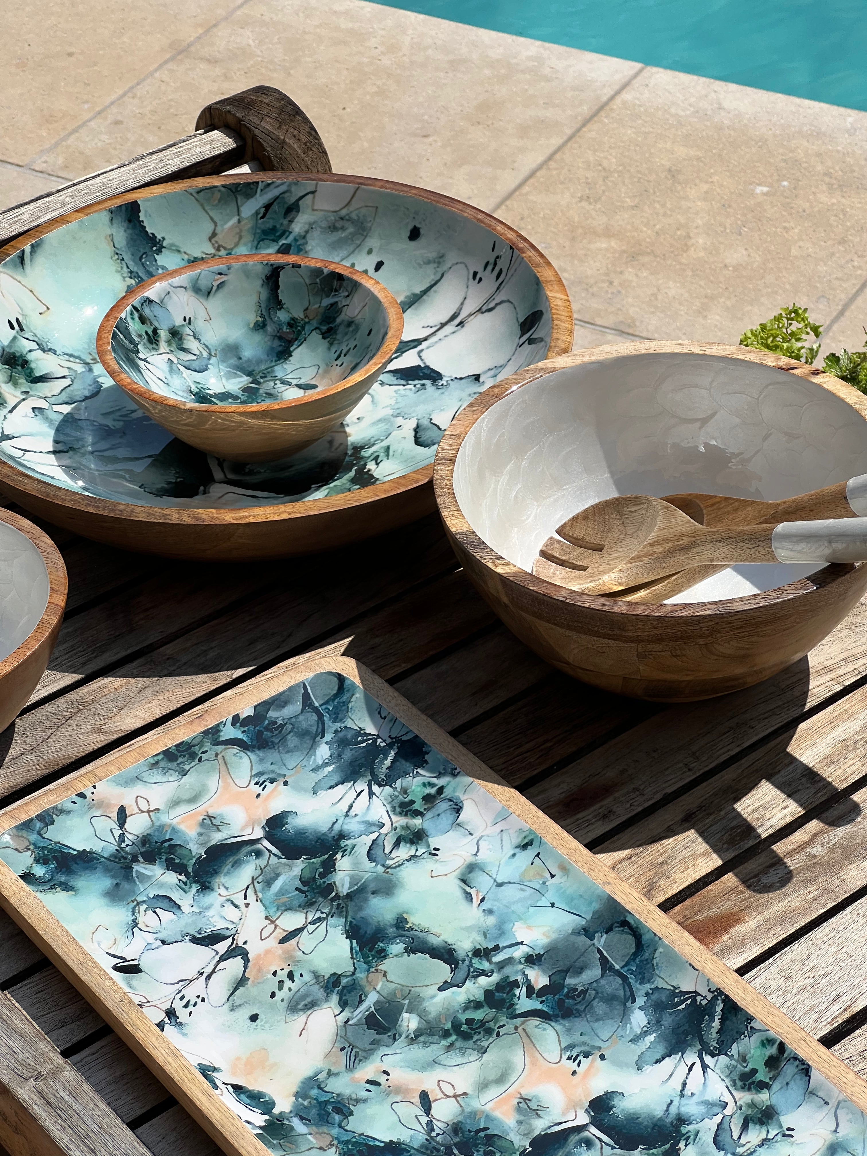 Medium sized white hand-painted  bowl with matching salad servers alongside a large and small blue marble decorated bowl and platter.  Made from sustainable mango wood with a food safe enamel coating