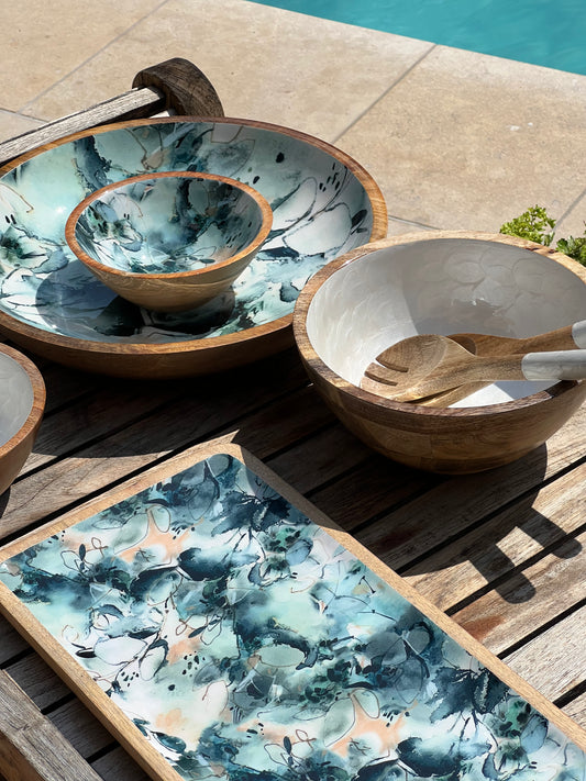 Medium sized white hand-painted  bowl with matching salad servers alongside a large and small blue marble decorated bowl and platter.  Made from sustainable mango wood with a food safe enamel coating