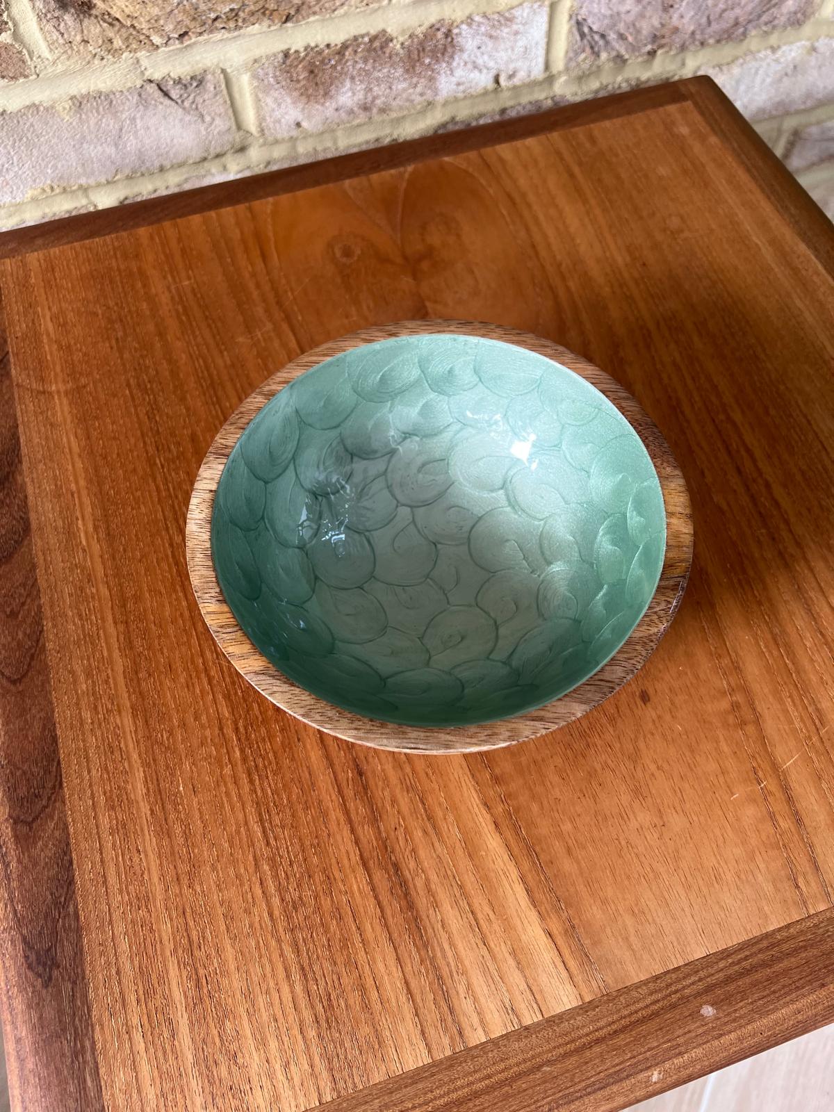 A small wooden bowl with a hand painted green tea coloured interior, set on a wooden table against a brick wall. Made from sustainable mango wood.  Small bowl suitable for snacks and nibbles.  Diameter 18cm.