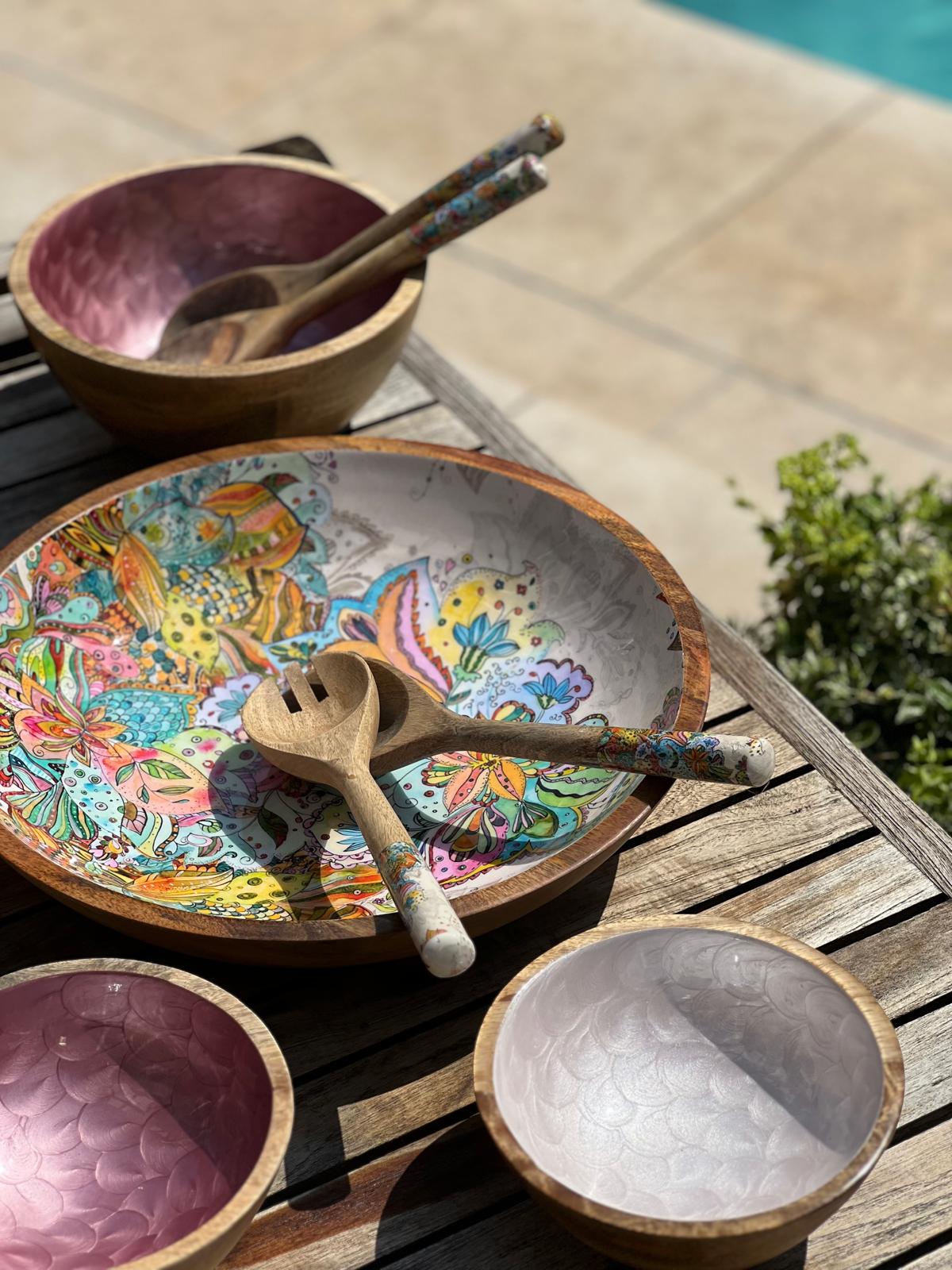 Colorful wooden bowl with multi-coloured floral design on a wooden surface outdoors.  With 3 hand-painted bowls in pinks and fish scales design