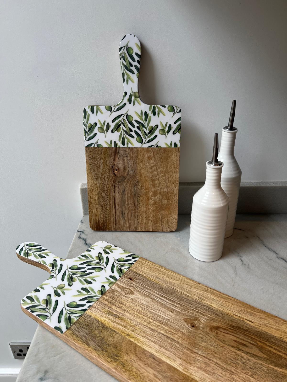 2 wooden serving boards with a white handle featuring a green olive branch pattern.  Made from sustainable mango wood.  In medium and large sizes. Suitable for use as a chopping, serving or cheese board.